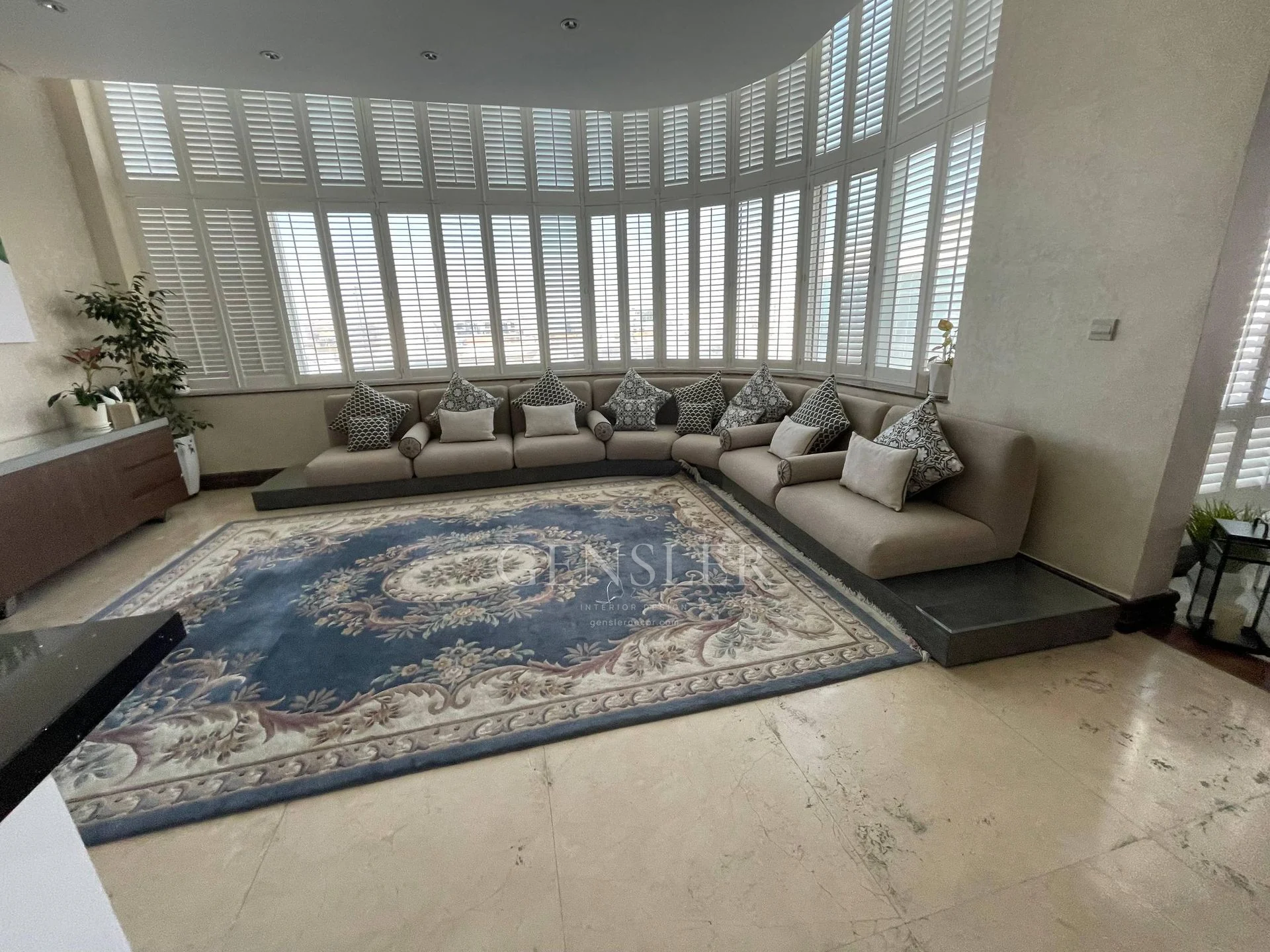 Wide lounge view with white shutters, neutral seating and a blue rug.
