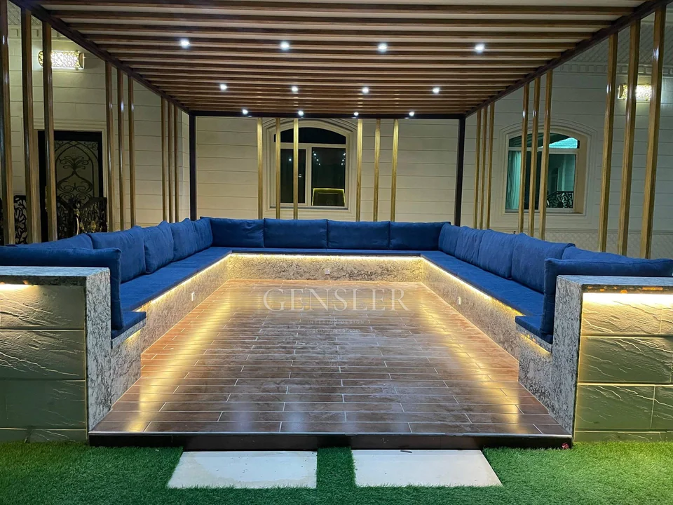 Blue outdoor majlis beneath a slatted canopy with warm base lighting.