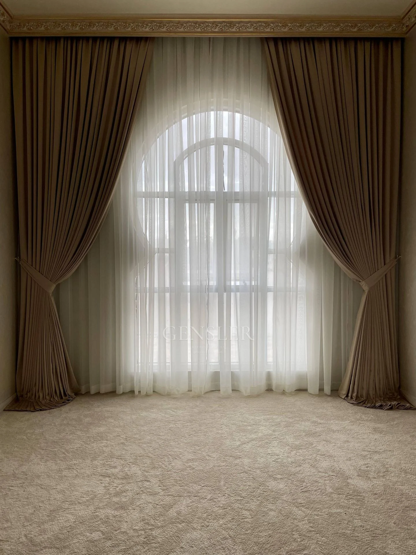 Brown gathered curtains and white sheers around an arched window.