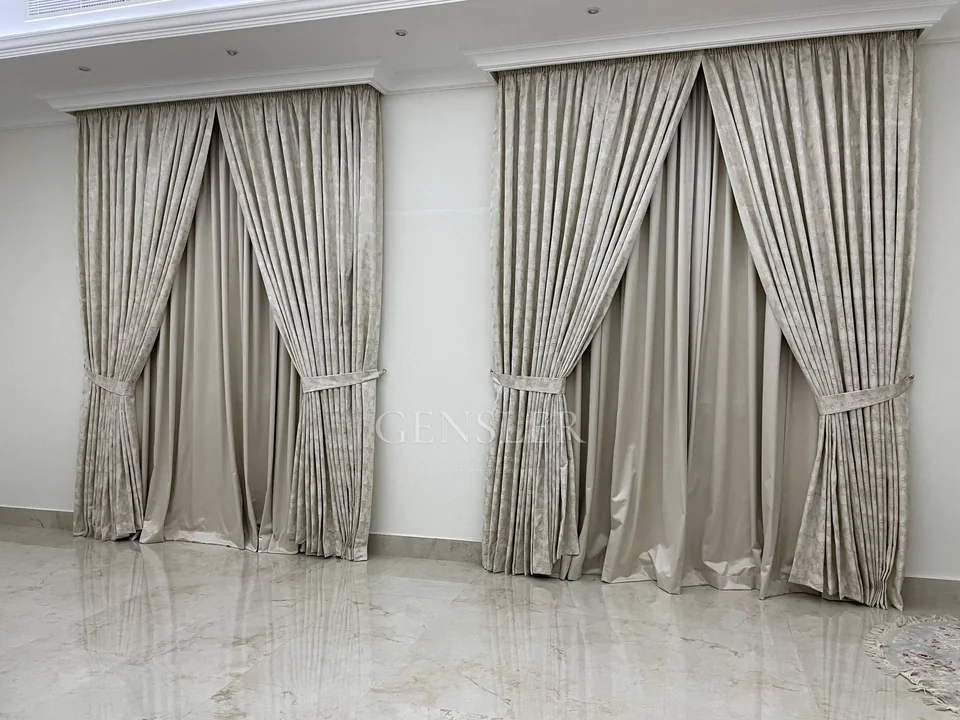 Silvery tied-back curtains with white sheers across tall windows.