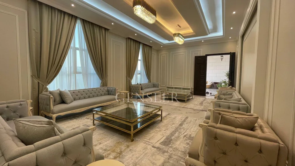Wide view of a formal majlis with pale tufted sofas and a large rug.
