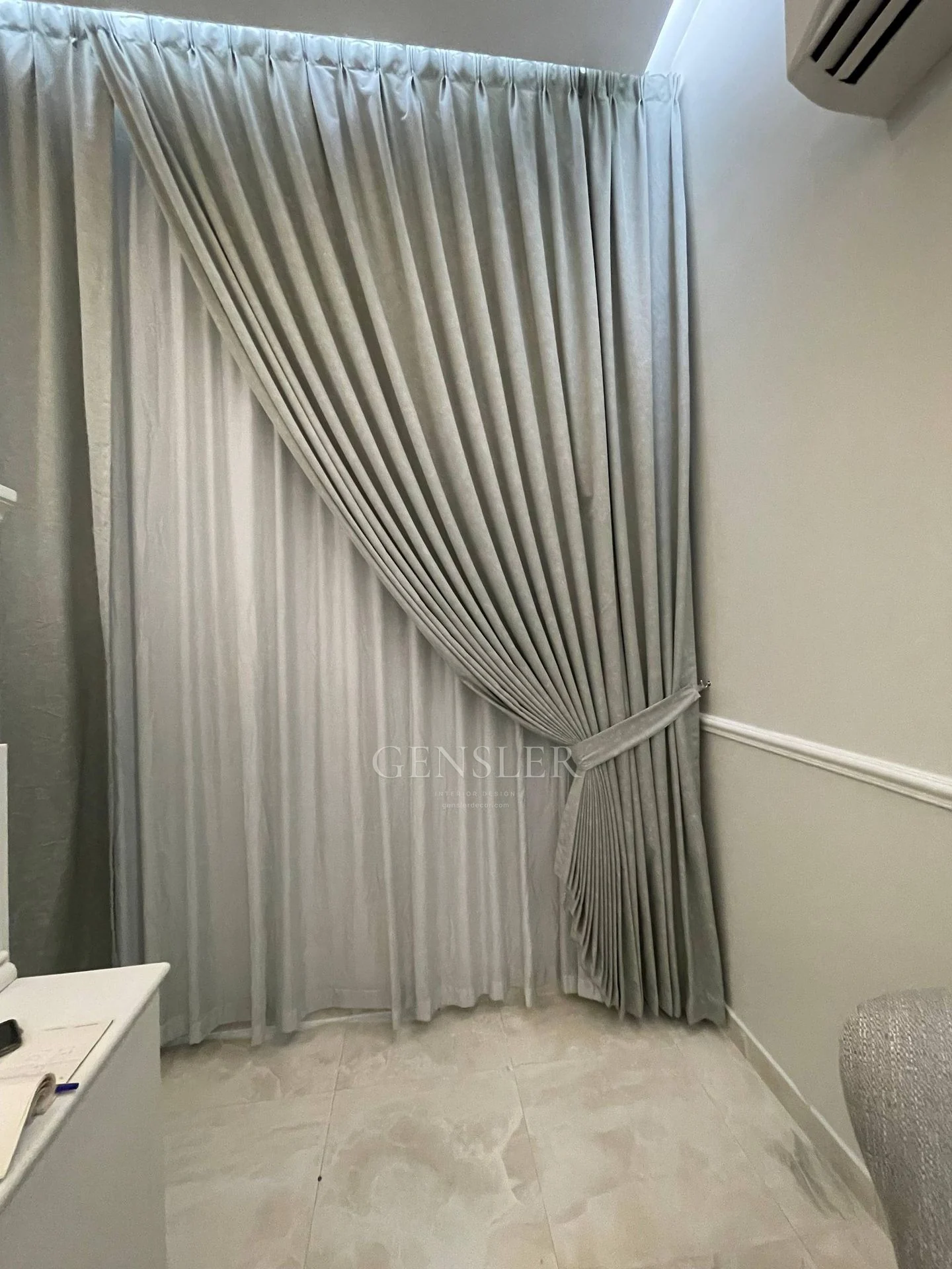 Neutral curtain gathered to one side over a sheer layer.