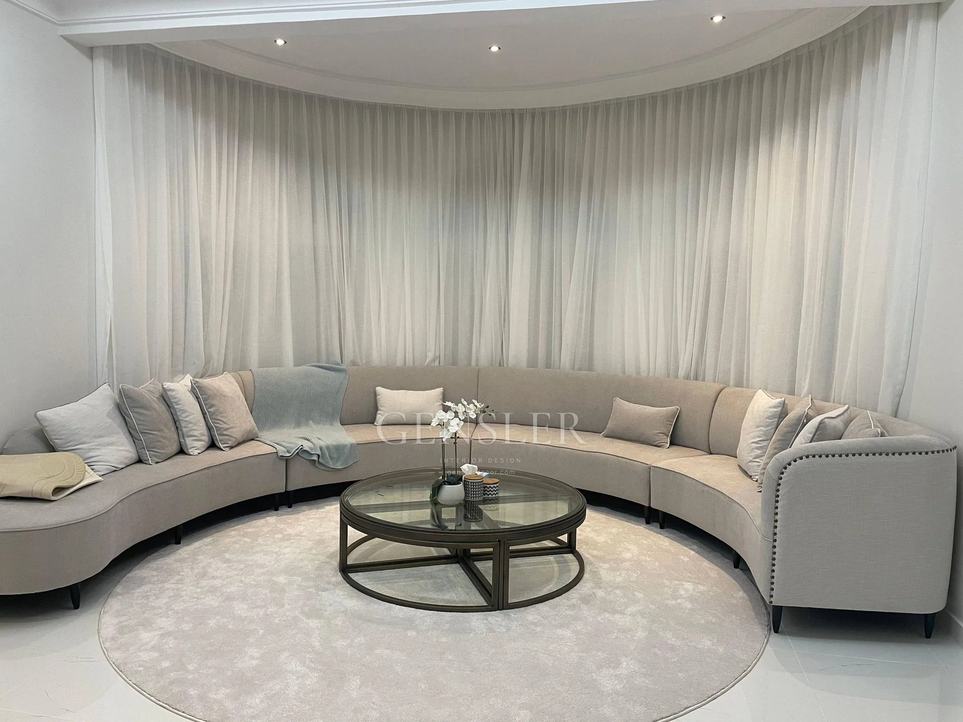 Curved ivory sofa around a circular rug and glass-top table.