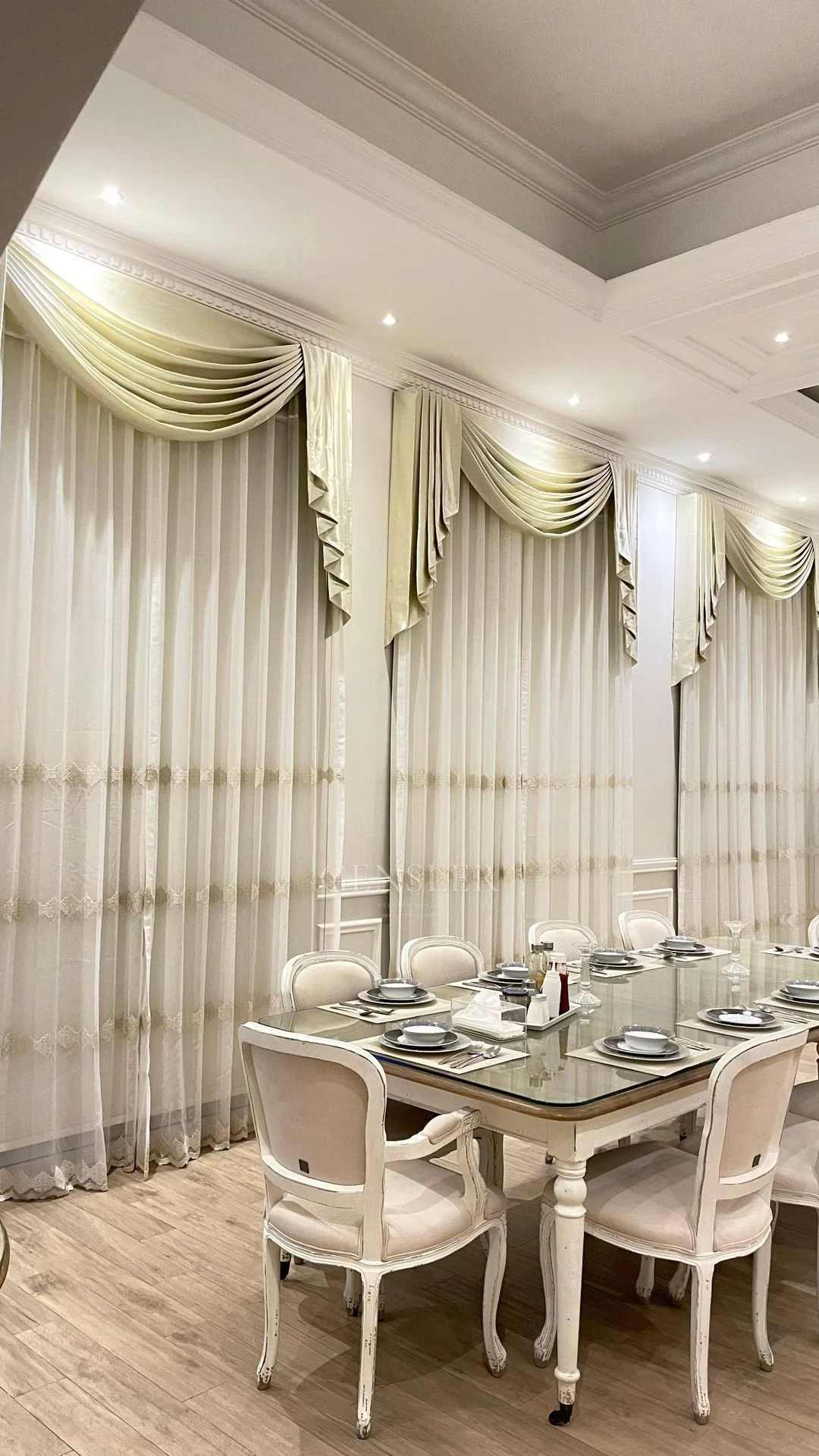 Classical dining chairs beside layered curtains with decorative swags.