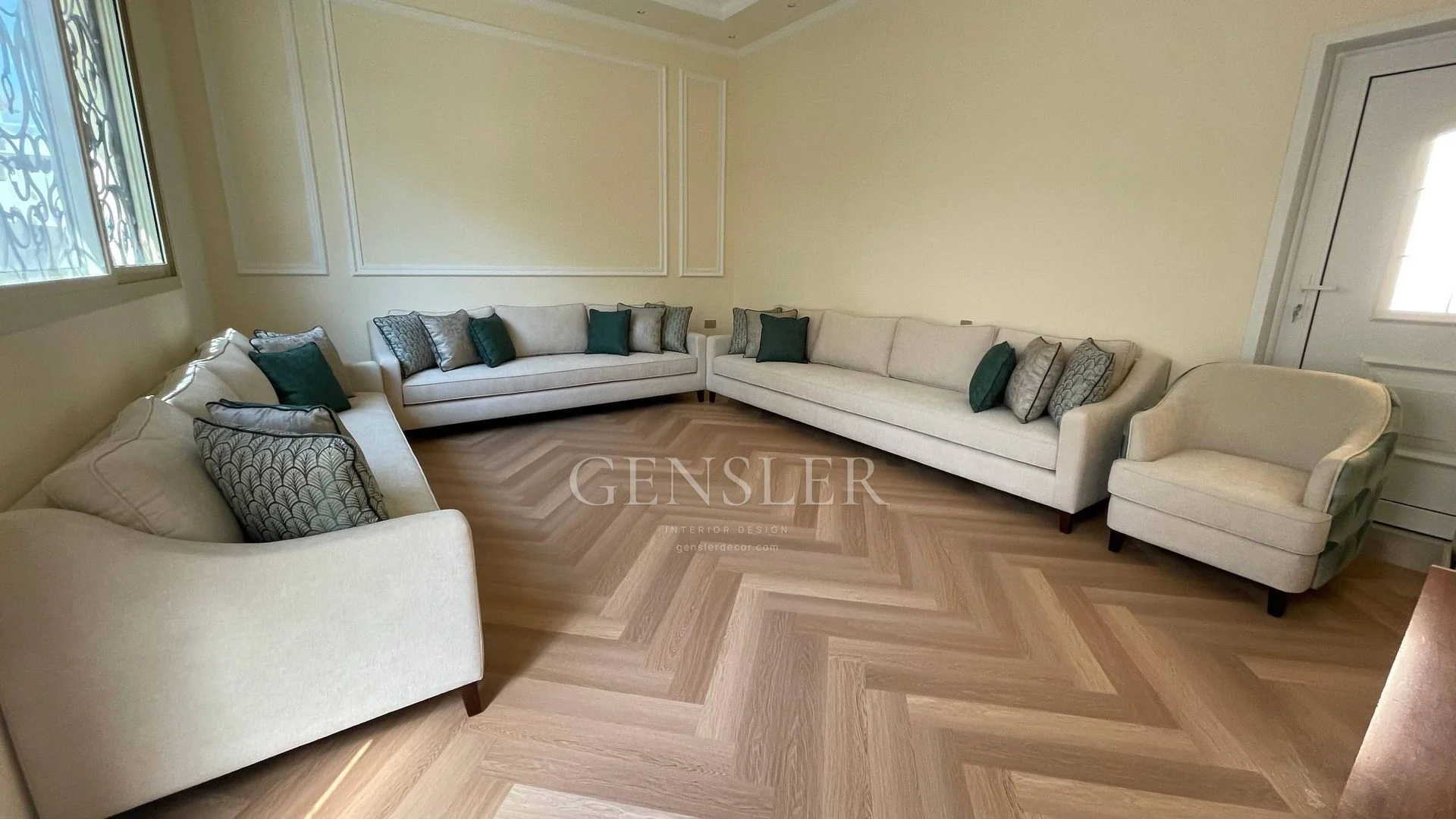 Cream sofas with green cushions on a herringbone-pattern floor.