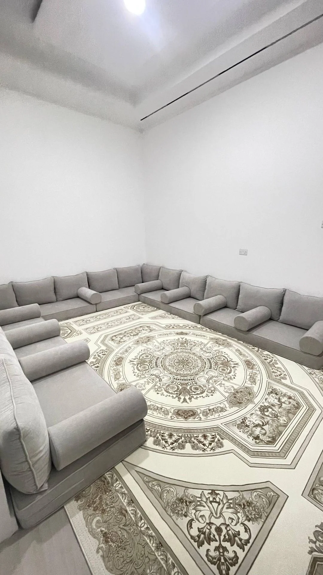 Portrait view of grey floor majlis seating and a medallion-pattern rug.