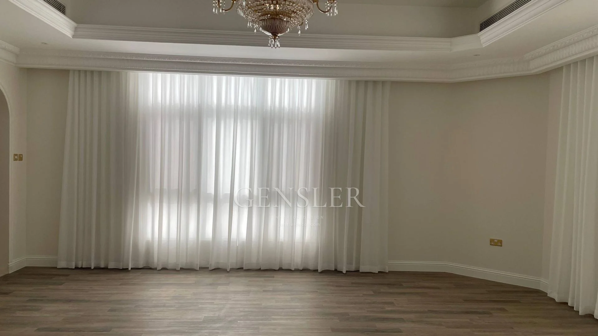 White sheers across a classical room with a chandelier and warm floor.
