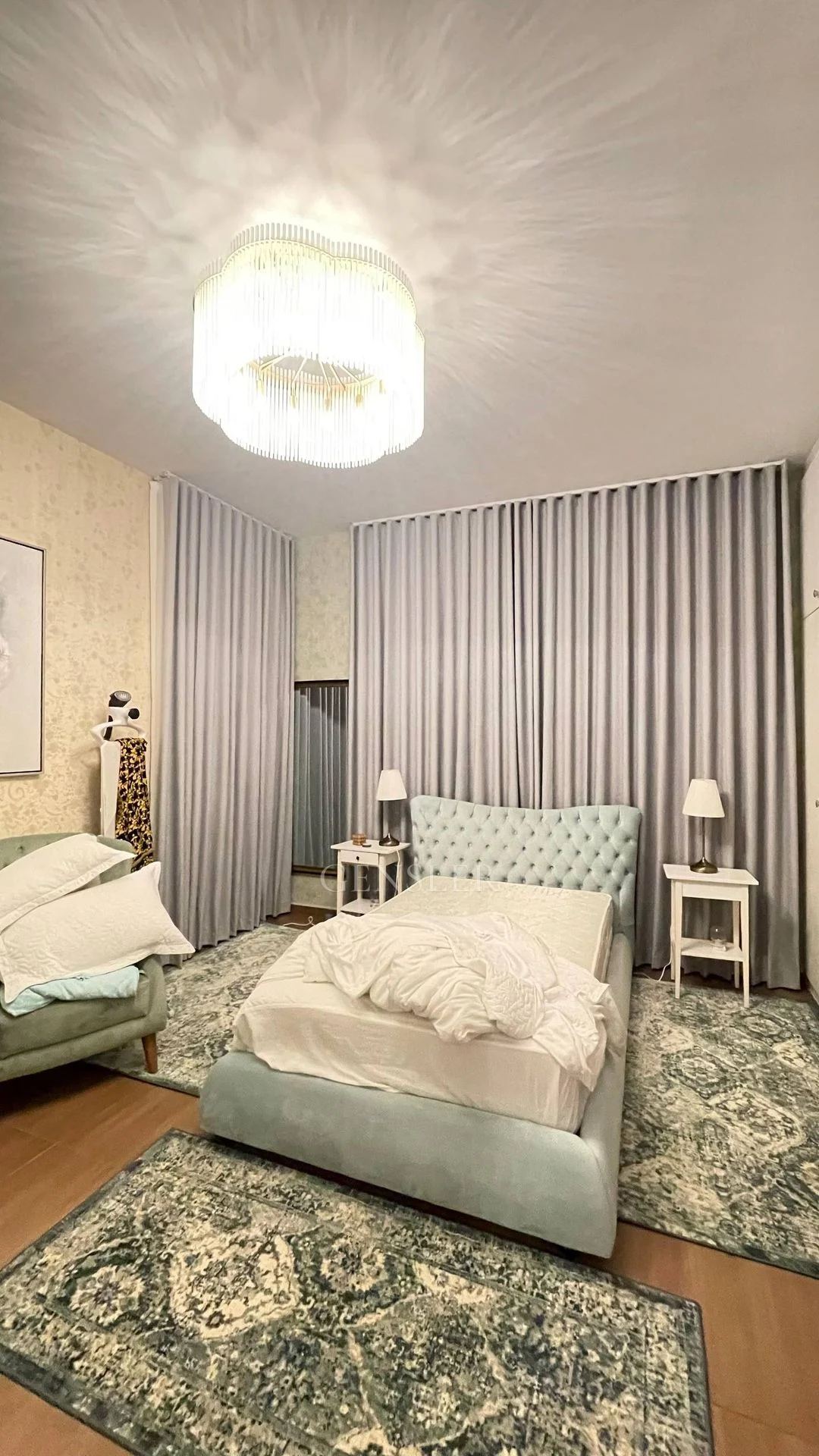 Pale blue upholstered beds with grey curtains and patterned rugs.