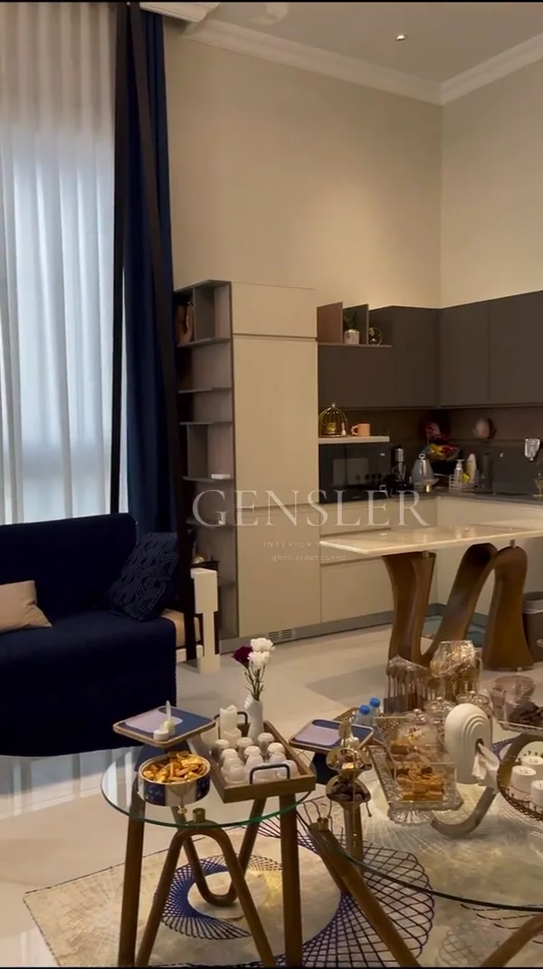 An overview of the living area and bedroom, with pale wall mouldings, rich blue accents and reflective details.